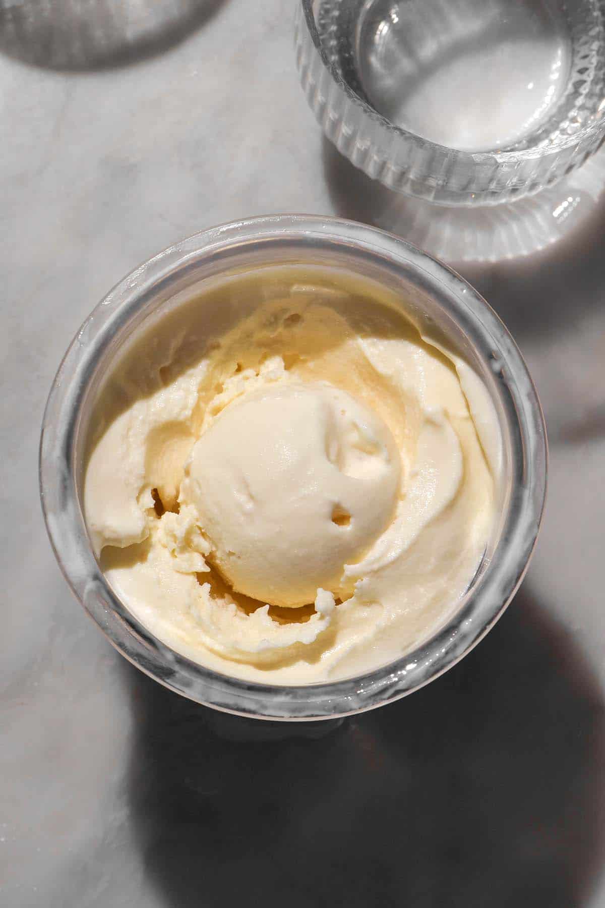 An aerial image of a tub of Ninja Creami frozen yoghurt on a white marble table in bright sunlight. 