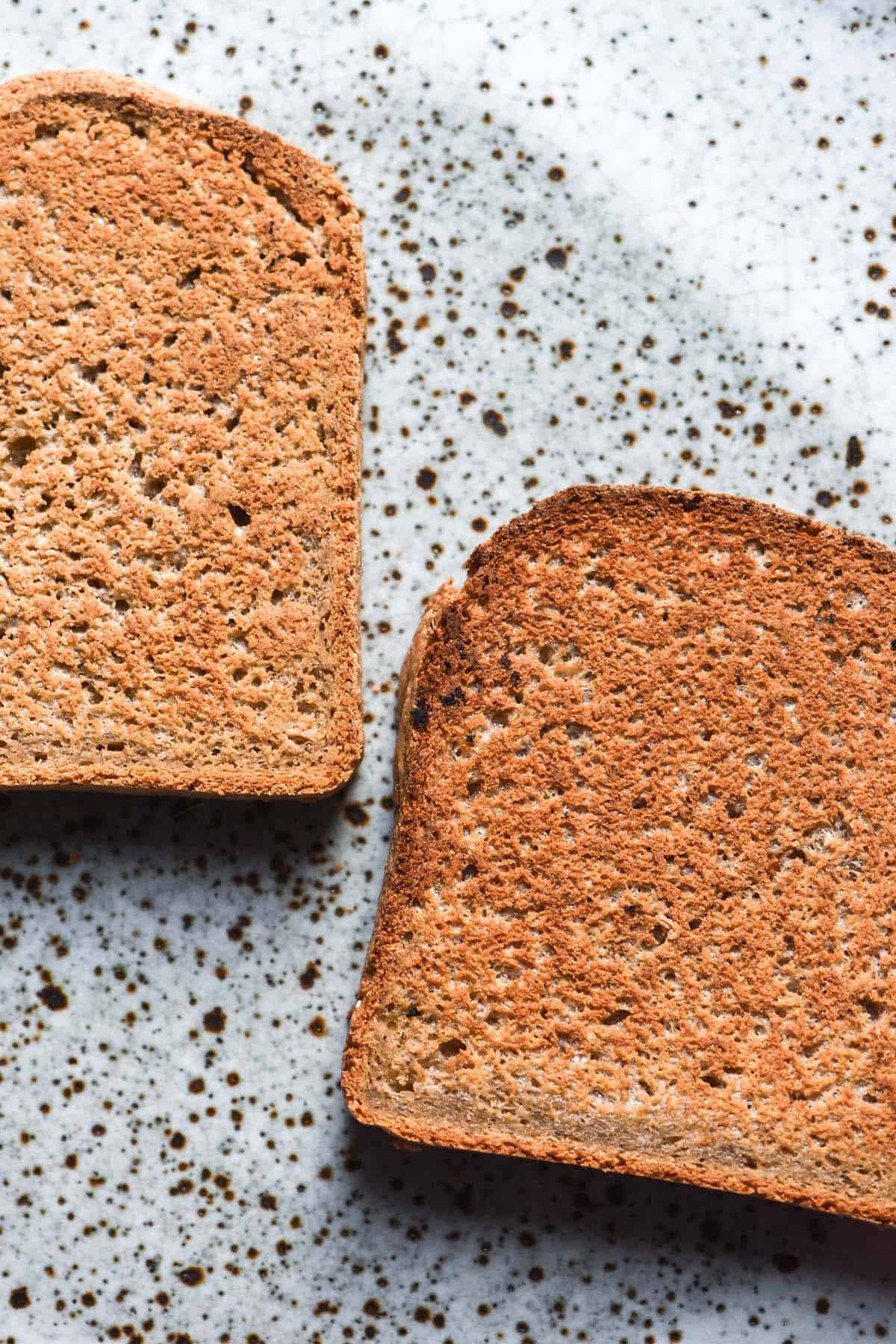 An aerial image of two slices of gluten free oat bread toast on a white speckled ceramic plate atop a white marble table