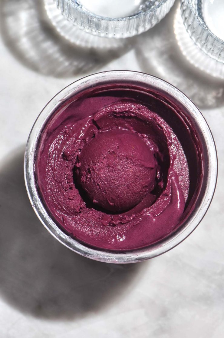 An aerial image of a tub of Ninja Creami açai bowl on a white marble table in bright sunlight.