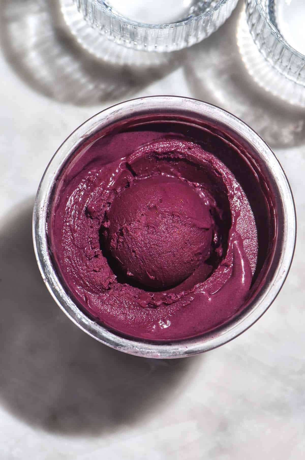 An aerial image of a tub of Ninja Creami açai bowl on a white marble table in bright sunlight.