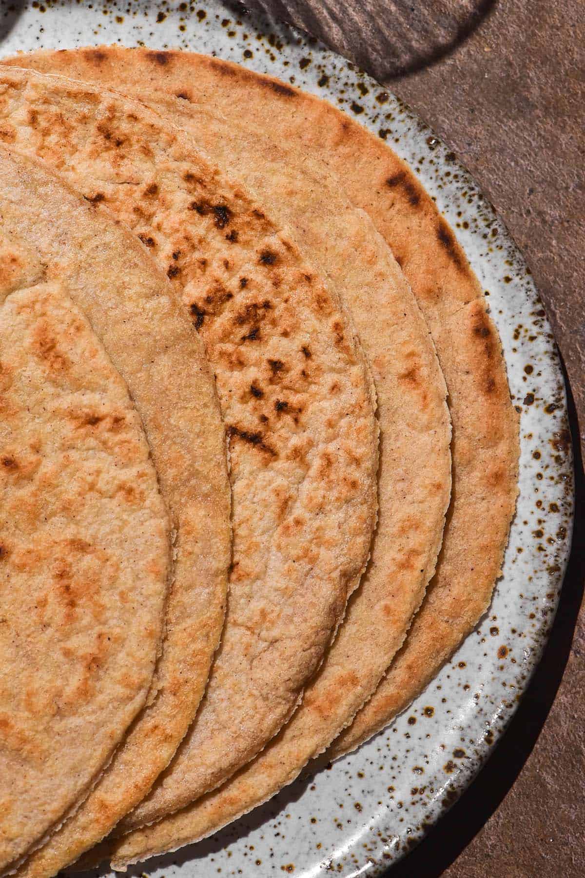 An aerial image of gluten free oat wraps fanned out on a white speckled ceramic plate atop a brown backdrop