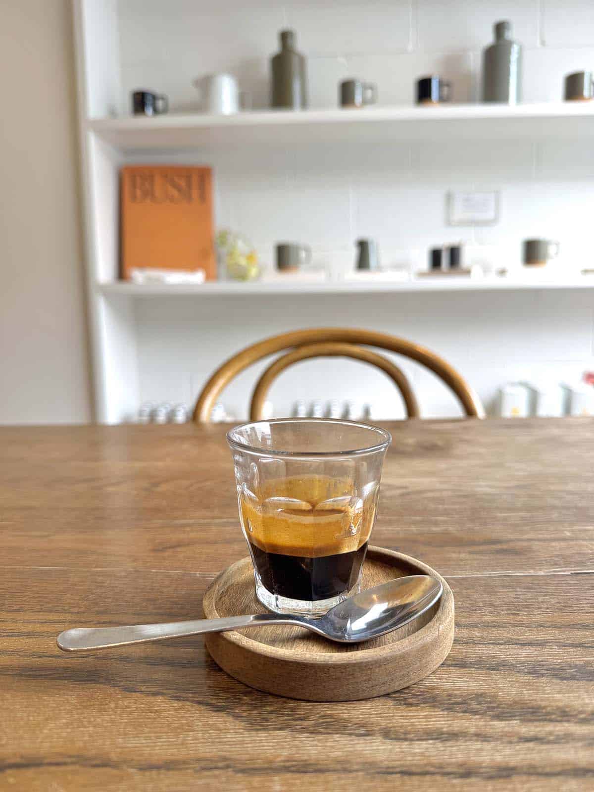 A side on image of an espresso on a wooden table with lined shelves behind it at Sunroom in Newstead Studios, Brisbane