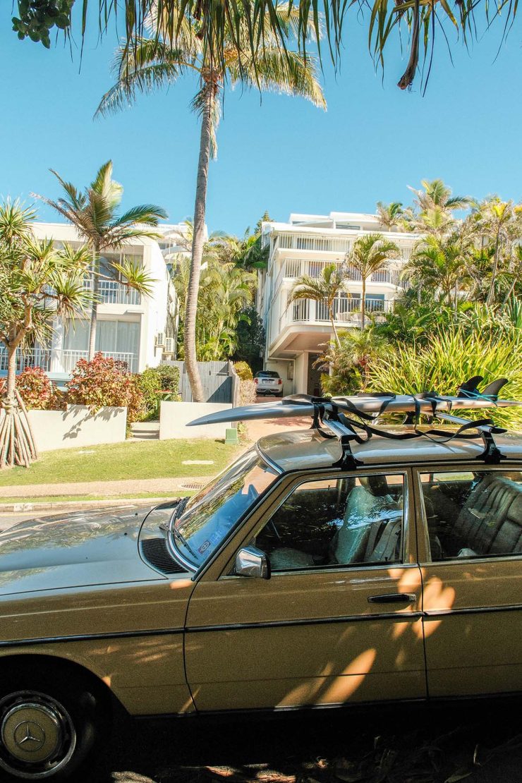 An image of a Noosa streetscape with an old car and a surfboard in the foreground