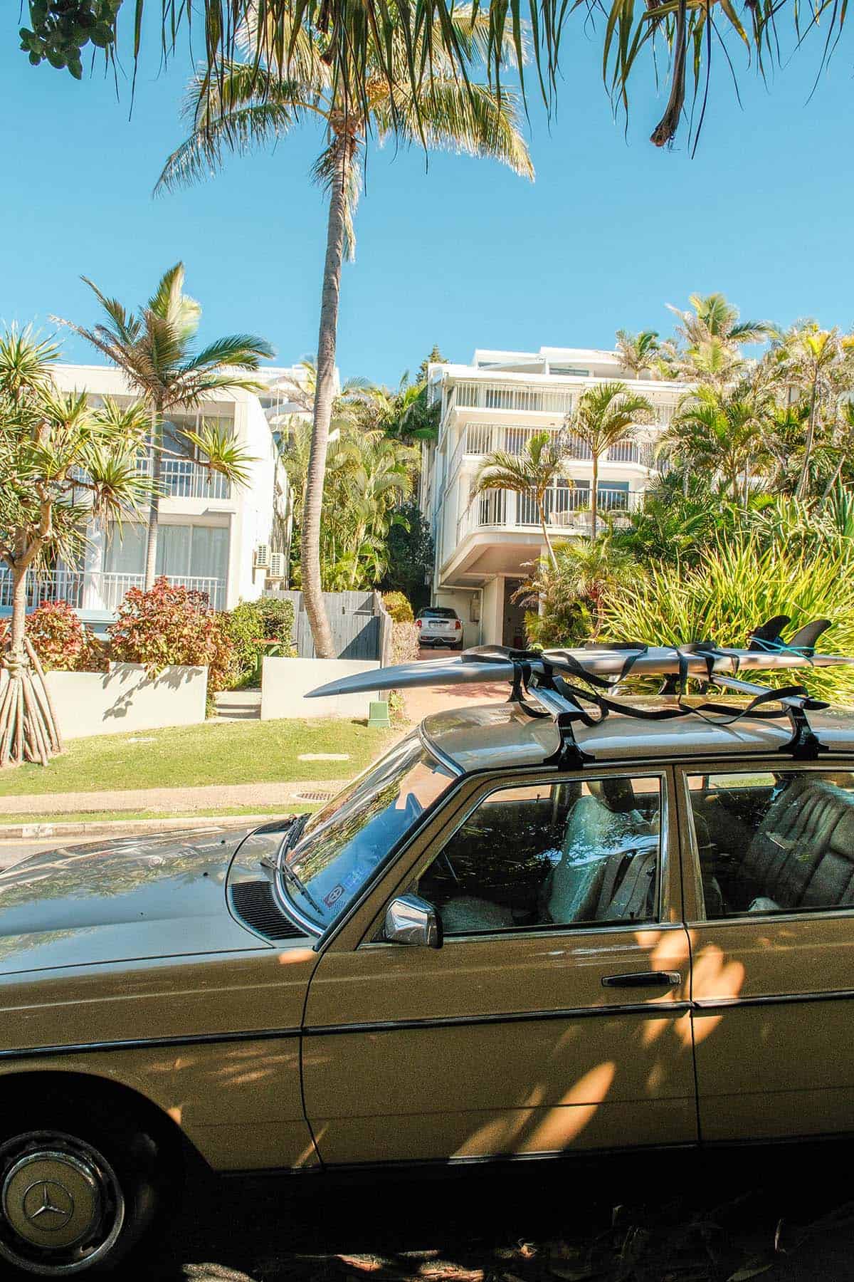 An image of a Noosa streetscape with an old car and a surfboard in the foreground
