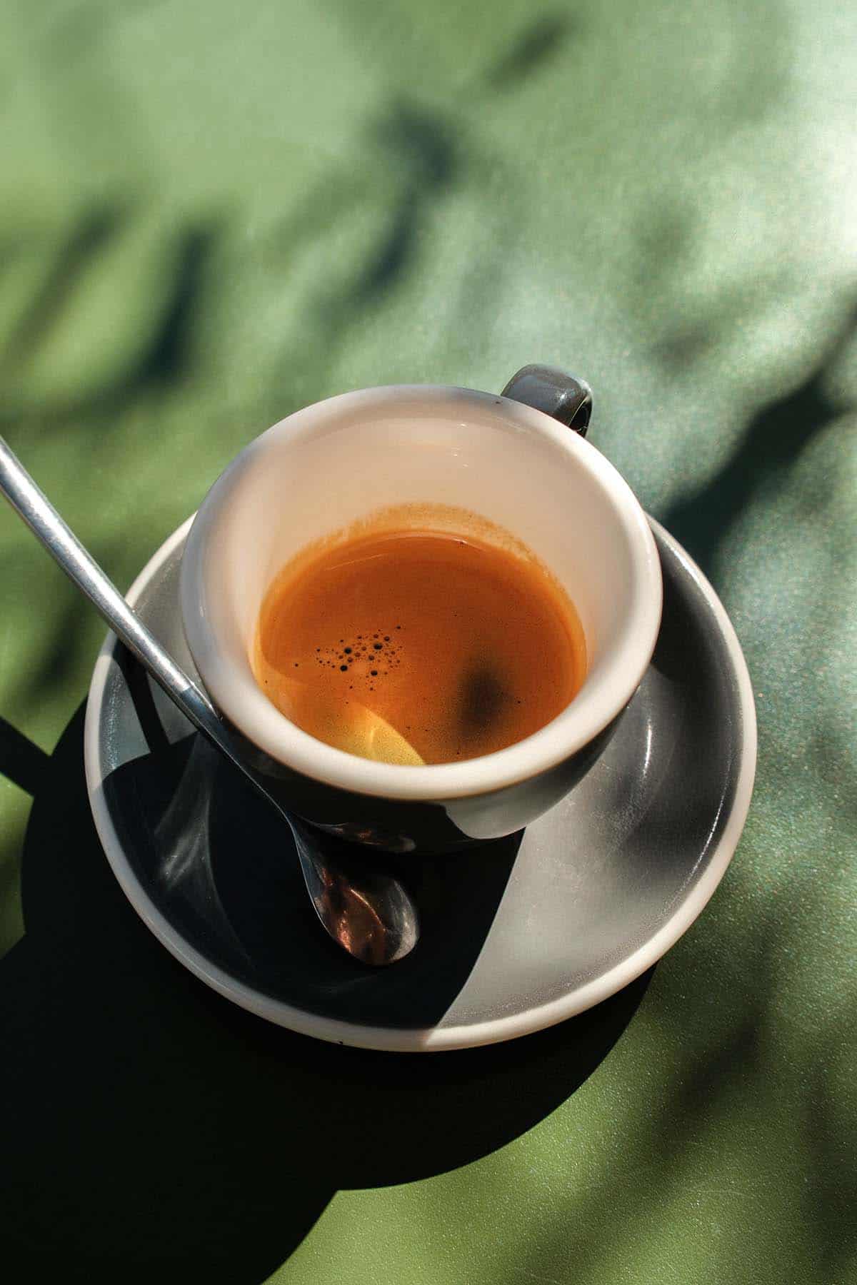 An image of an espresso and saucer on an olive green table in dappled sunlight at Vanilla Foods in Noosa. 