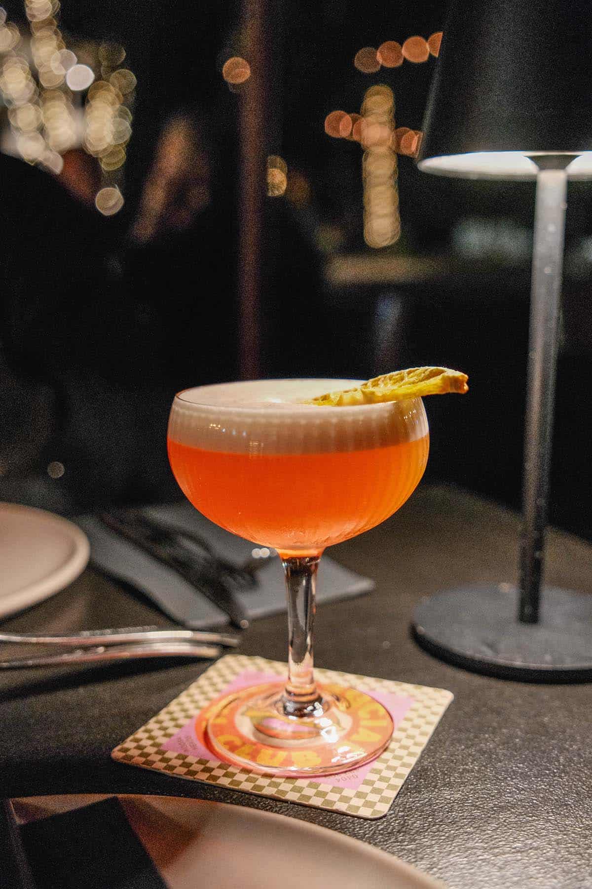 A dark and moody image of a pink cocktail with fairy lights in the background at Theo's Social Club in Noosa, Australia