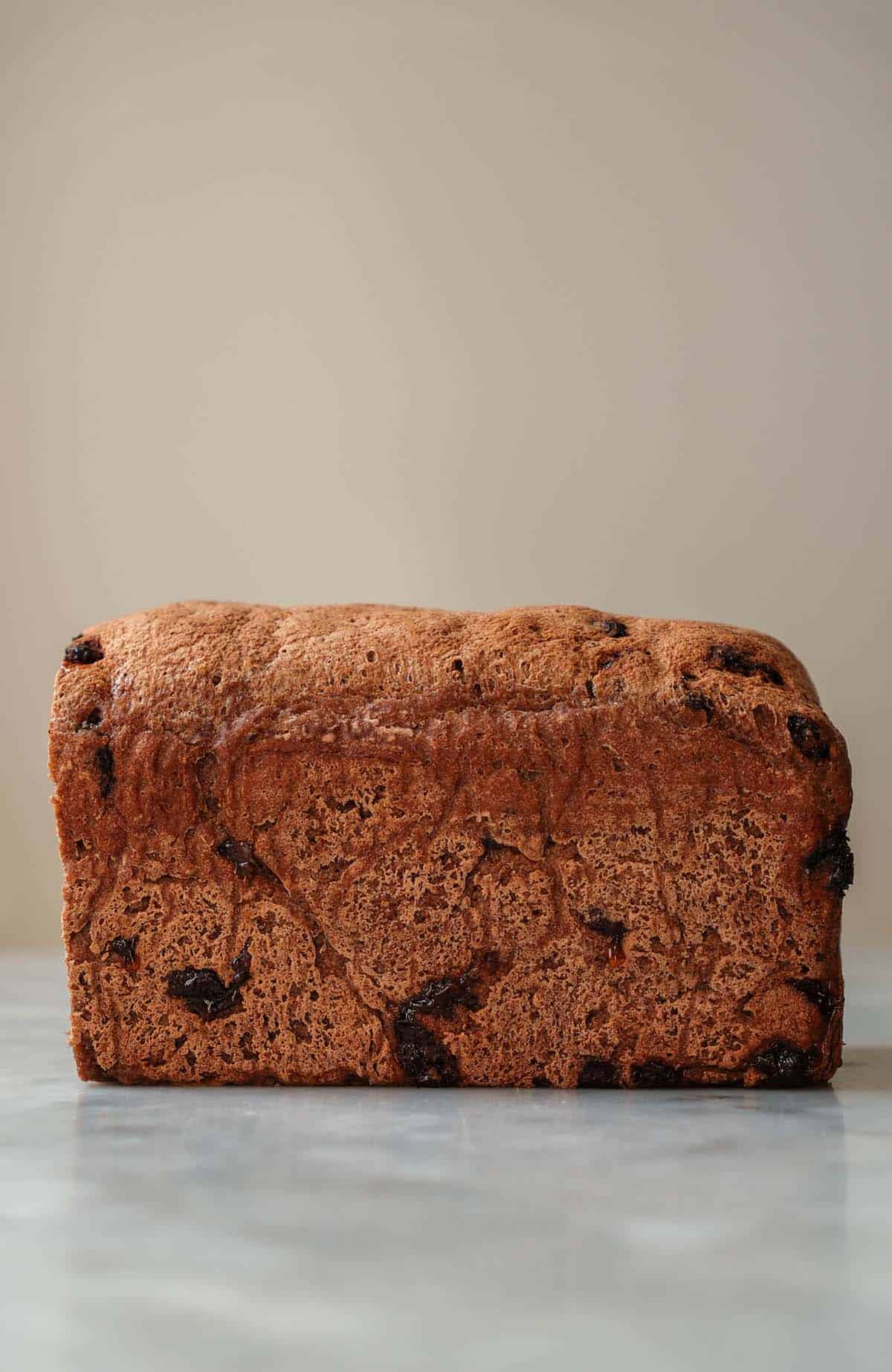 A side on image of a loaf of gluten free cinnamon raisin bread on a white marble table against a white backdrop