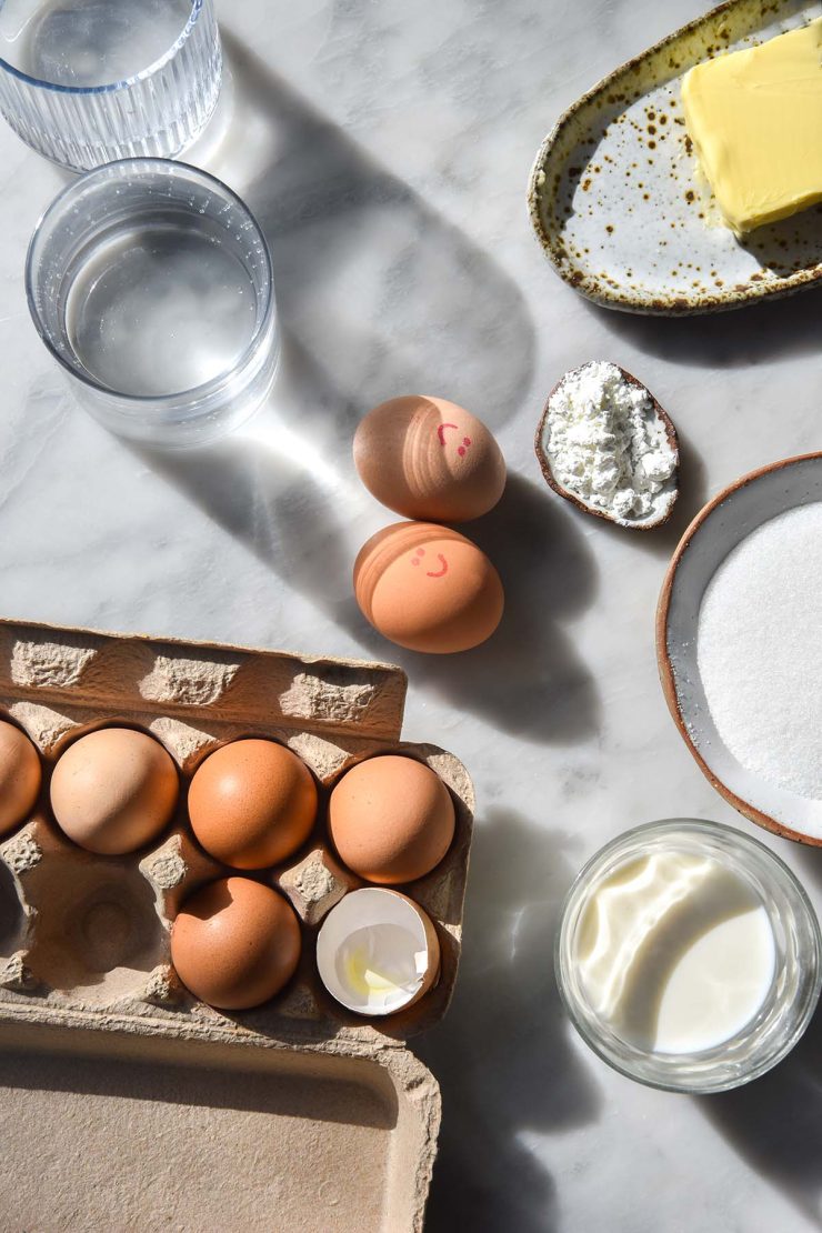An aerial image of the ingredients used to make lactose free pastry cream casually arranged on a sunlit marble table