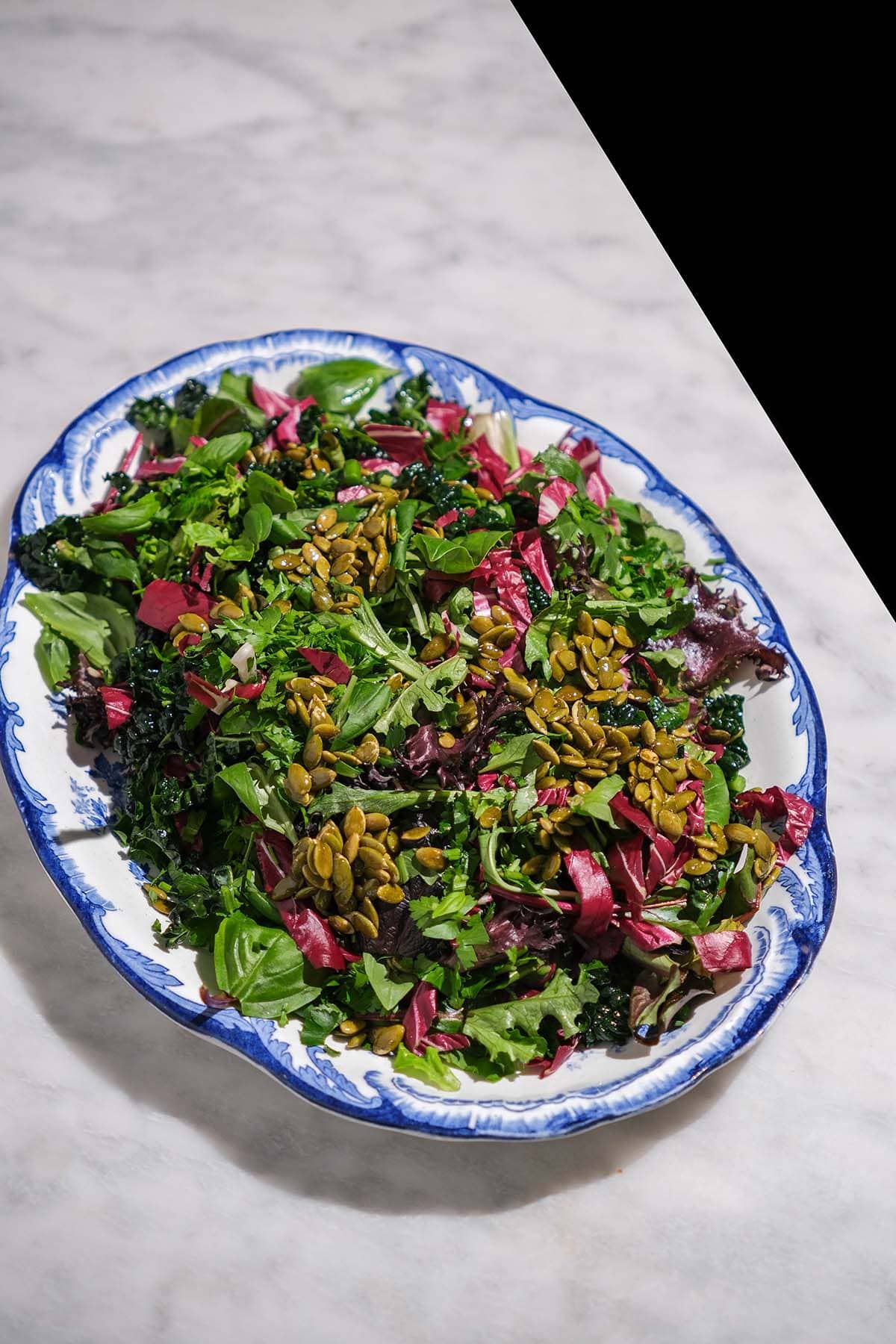 An aerial image of a low histamine salad on a blue and white scalloped plate atop a white marble table. 
