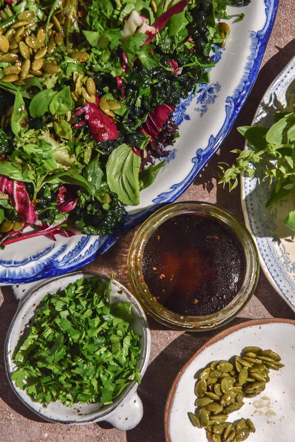 An aerial image of a small jar of low histamine salad dressing surrounded by a low histamine salad and small bowls of ingredients used on the salad. 
