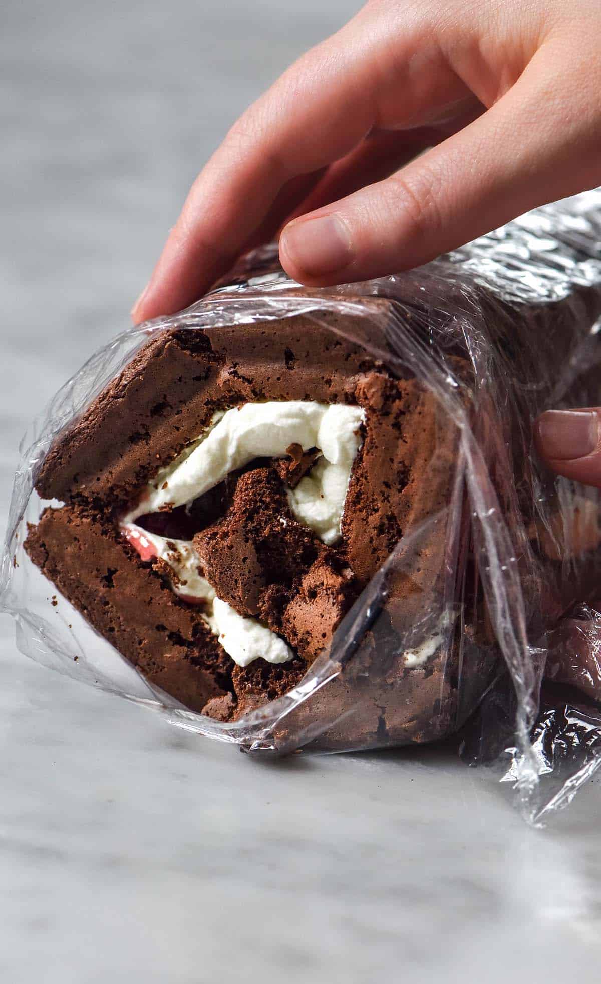 An image of a gluten free chocolate roulade being rolled up on a white marble table