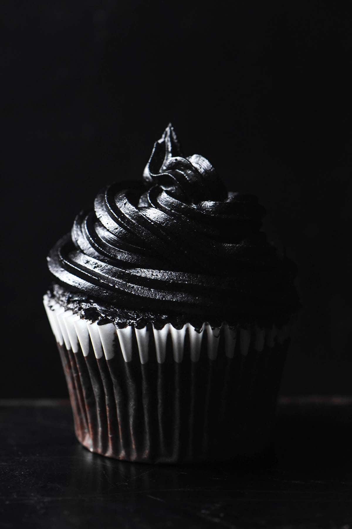 A macro side on image of a cupcake topped with a swirl of black buttercream against a black backdrop