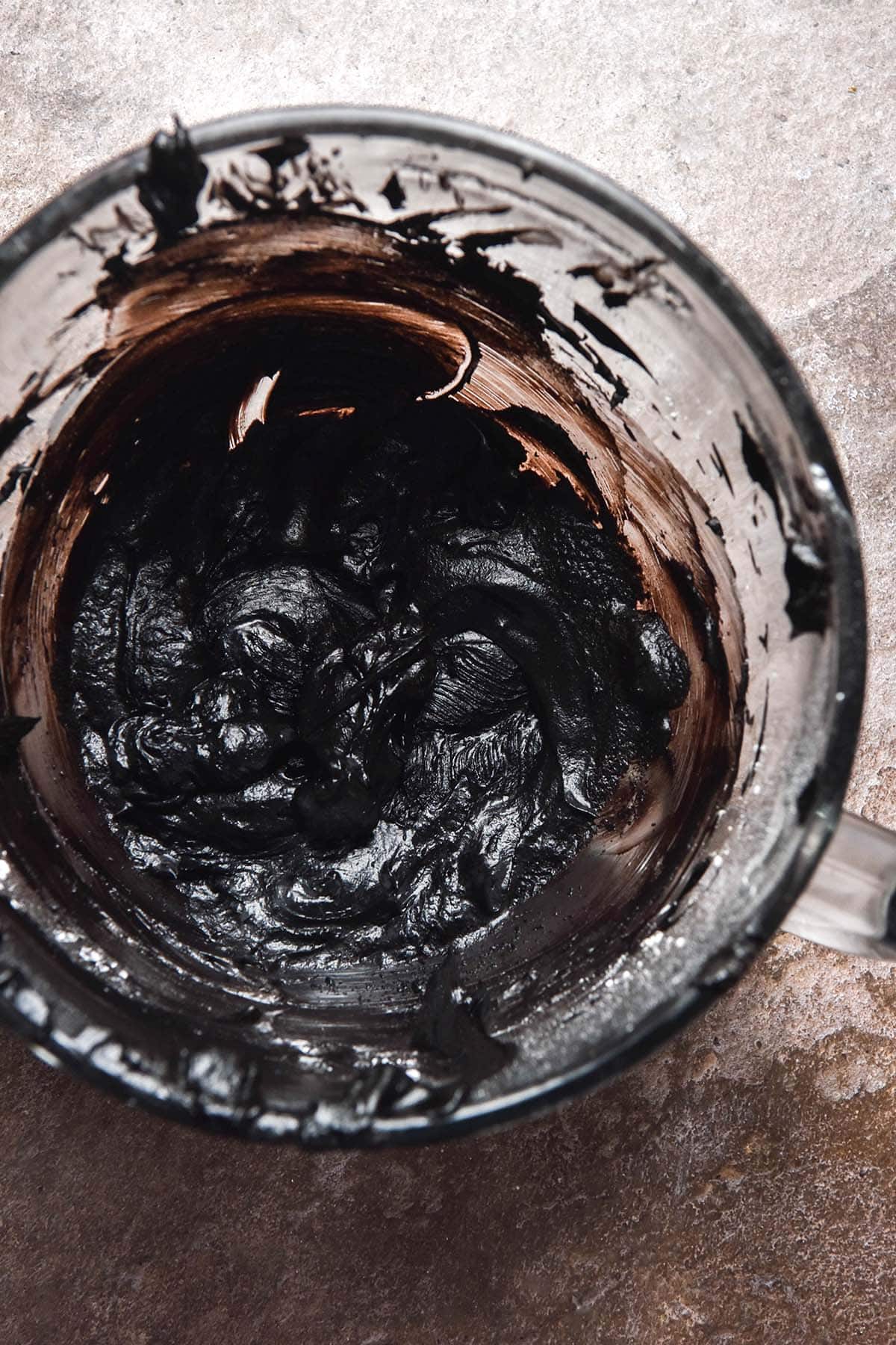 An aerial image of a glass KitchenAid bowl filled with black buttercream on a brown backdrop