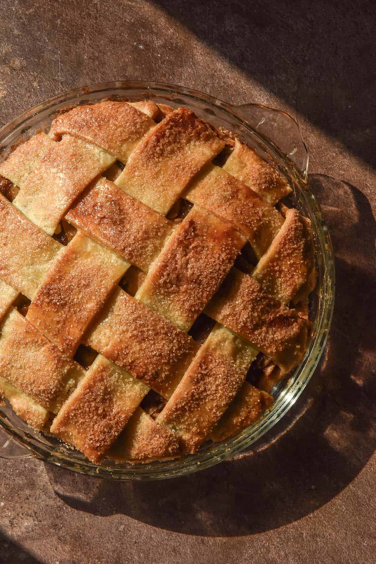 An aerial sunlight image of a gluten free lattice apple pie on a brown backdrop in contrasting sunlight