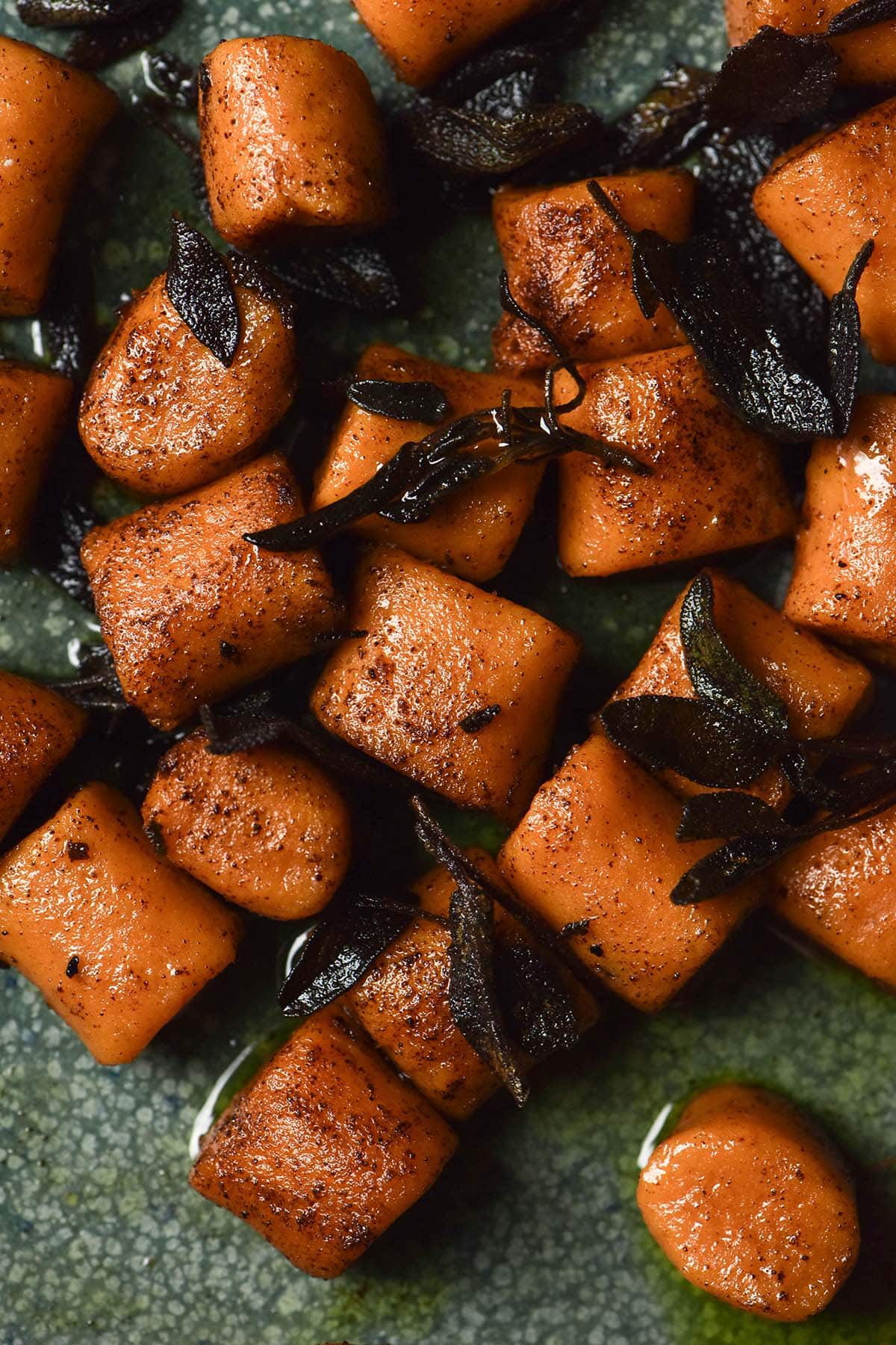 An aerial moody image of gluten free sweet potato gnocchi in brown butter sage sauce on a green ceramic plate.