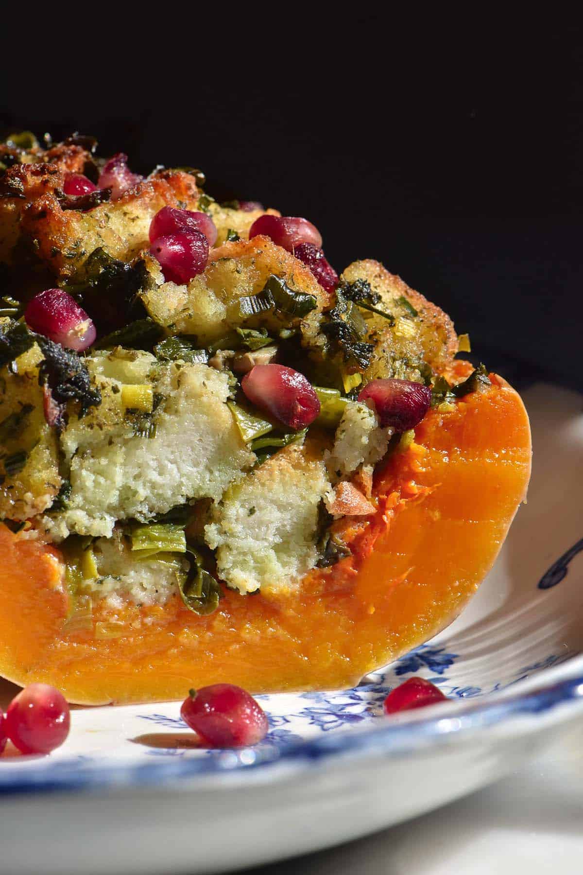 A side on image of a stuffing filled pumpkin on a white and blue ceramic plate against a dark backdrop. The pumpkin has been sliced to reveal the inside flesh.