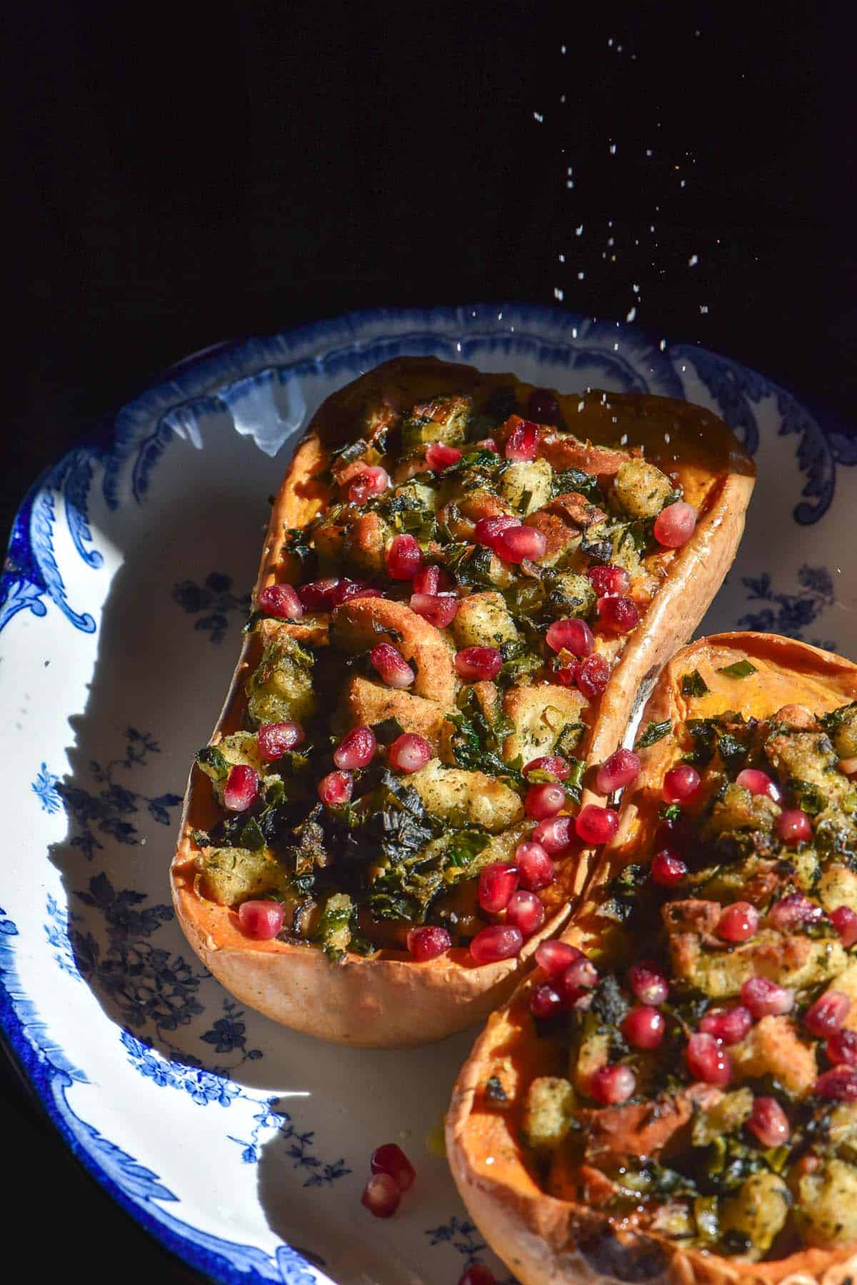 A moody image of low FODMAP stuffed pumpkin being sprinkled with salt against a dark backdrop