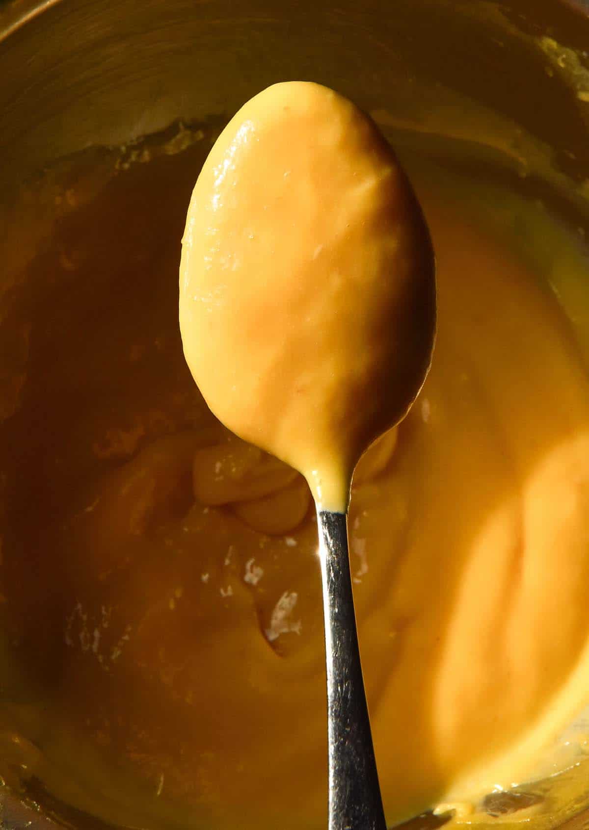 An aerial macro image of a spoon of mango curd sitting over the bowl.