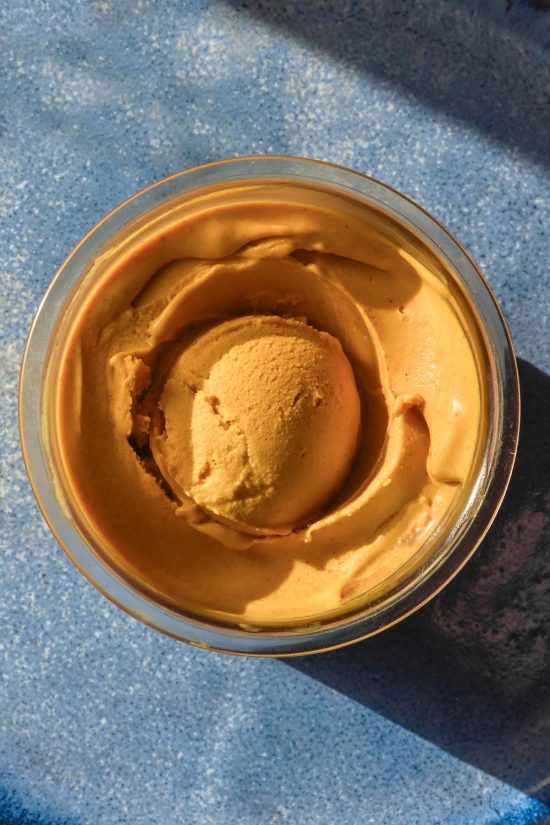 A brightly lit aerial image of a tub of vegan Ninja Creami pumpkin ice cream on a bright blue ceramic plate