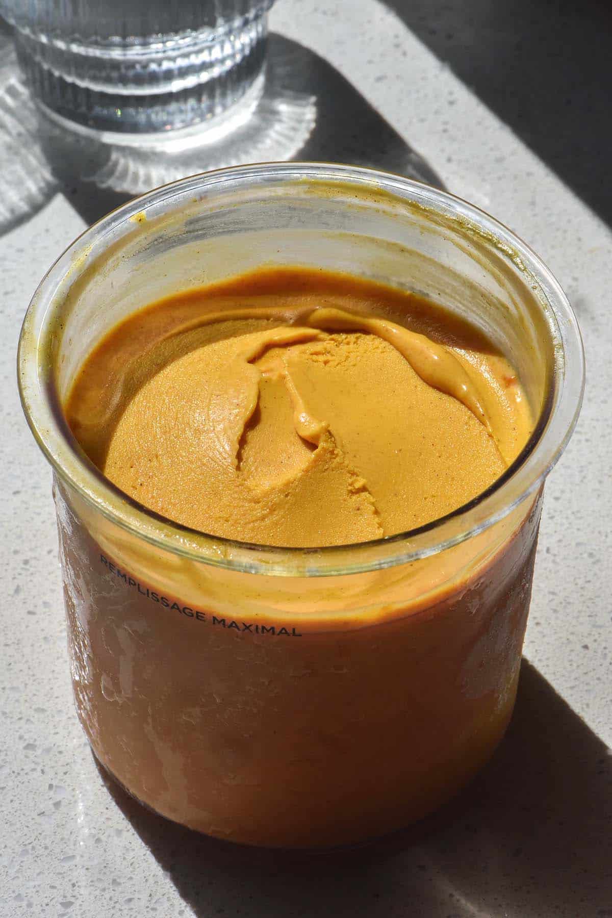 A sunlit image of a tub of pumpkin spice Ninja Creami ice cream on a white stone bench in contrasting sunlight. 