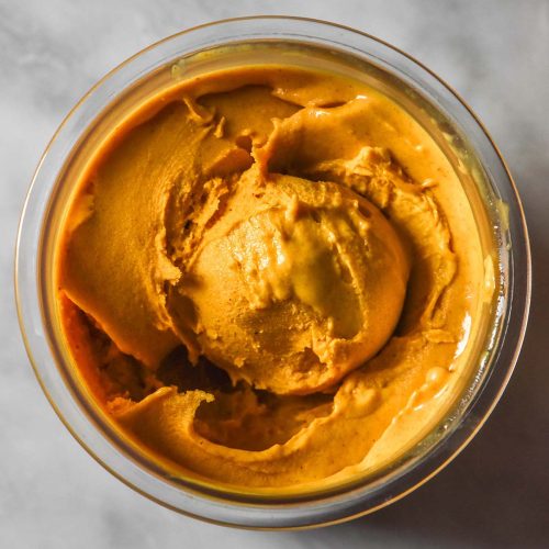 An aerial image of a tub of pumpkin maple Ninja creami ice cream on a white marble table