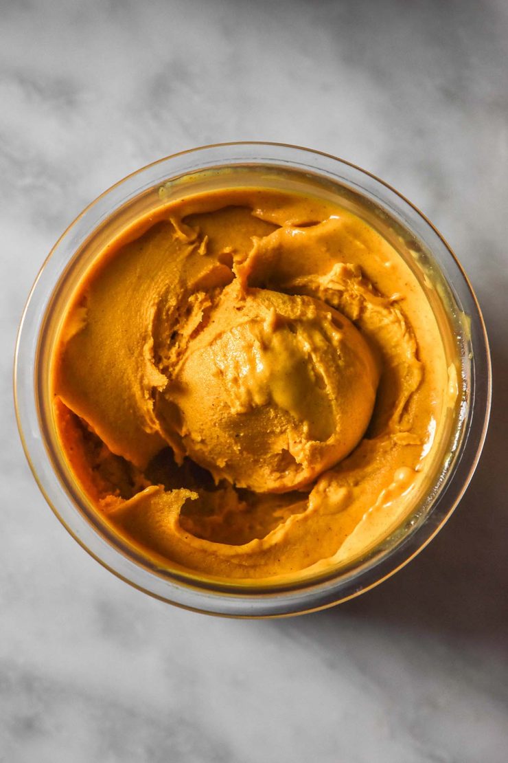 An aerial image of a tub of pumpkin maple Ninja creami ice cream on a white marble table