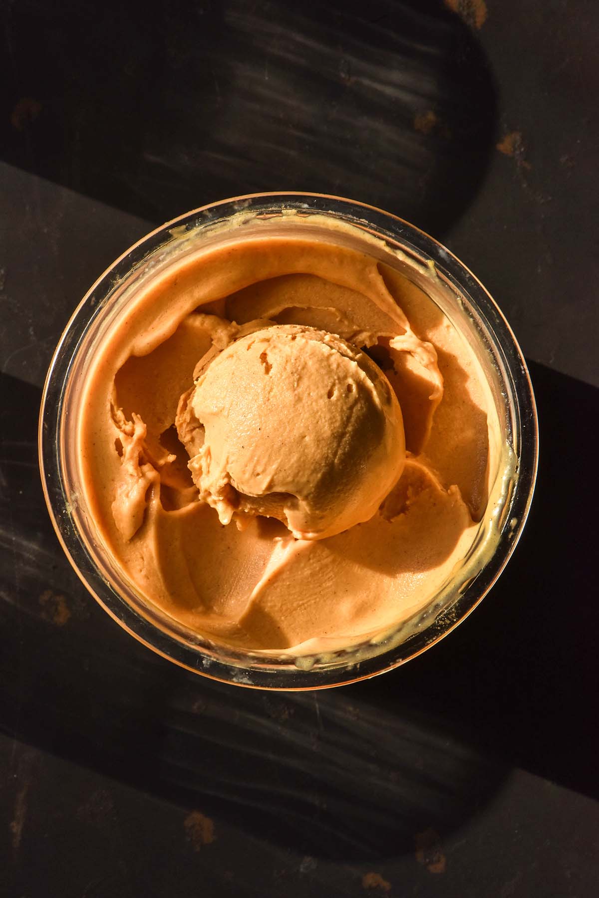 An aerial image of a tub of sweet potato Ninja creami ice cream on a black backdrop in bright sunlight