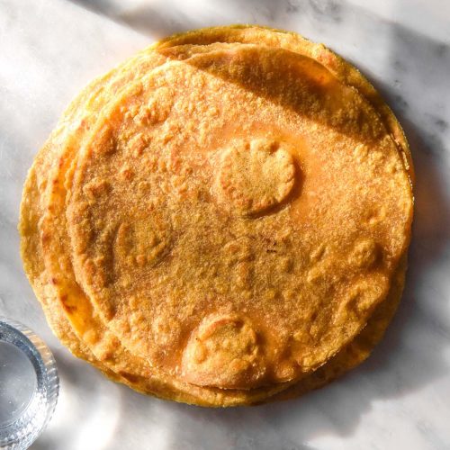 A brightly lit aerial image of a stack of gluten free sweet potato tortillas on a white marble table. Glasses of water cast shadows to the top and bottom of the tortillas
