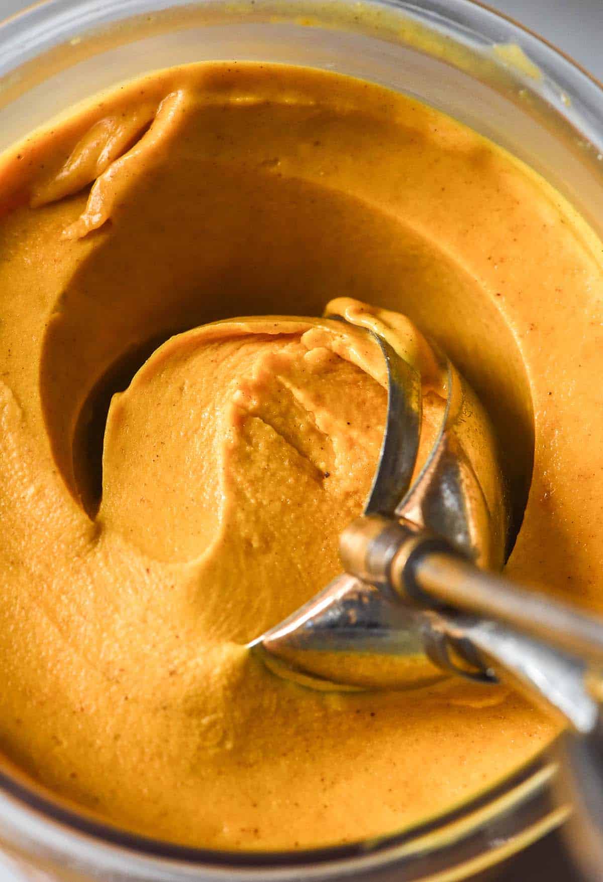 A macro close up image of a tub of vegan pumpkin Ninja Creami. An ice cream scoop digs into the ice cream in the centre of the tub