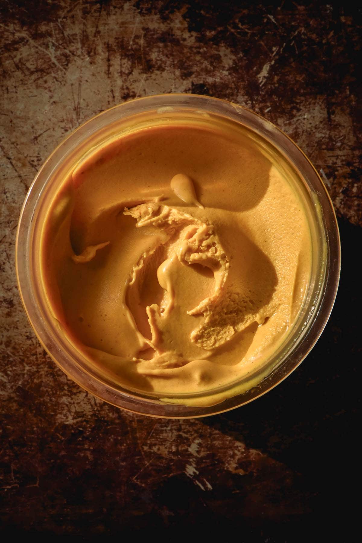 An aerial image of a tub of pumpkin Ninja Creami ice cream on a dark grey mottled backdrop