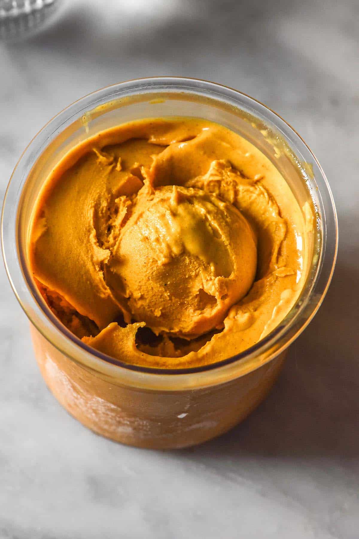 An aerial image of a tub of pumpkin maple Ninja creami ice cream on a white marble table