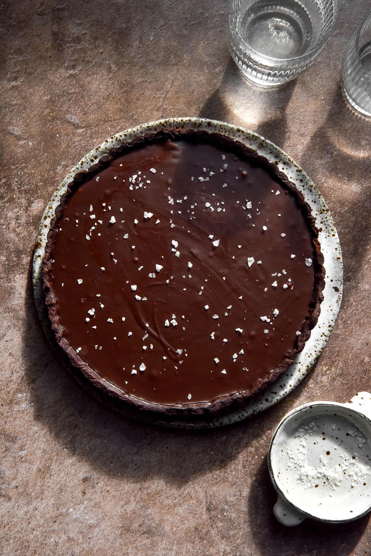 An aerial image of a gluten free chocolate tart sprinkled with sea salt flakes atop a light brown backdrop