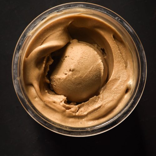 An aerial image of a tub of Ninja Creami vegan gingerbread ice cream on a black backdrop. The ice cream has a scoop in the centre.
