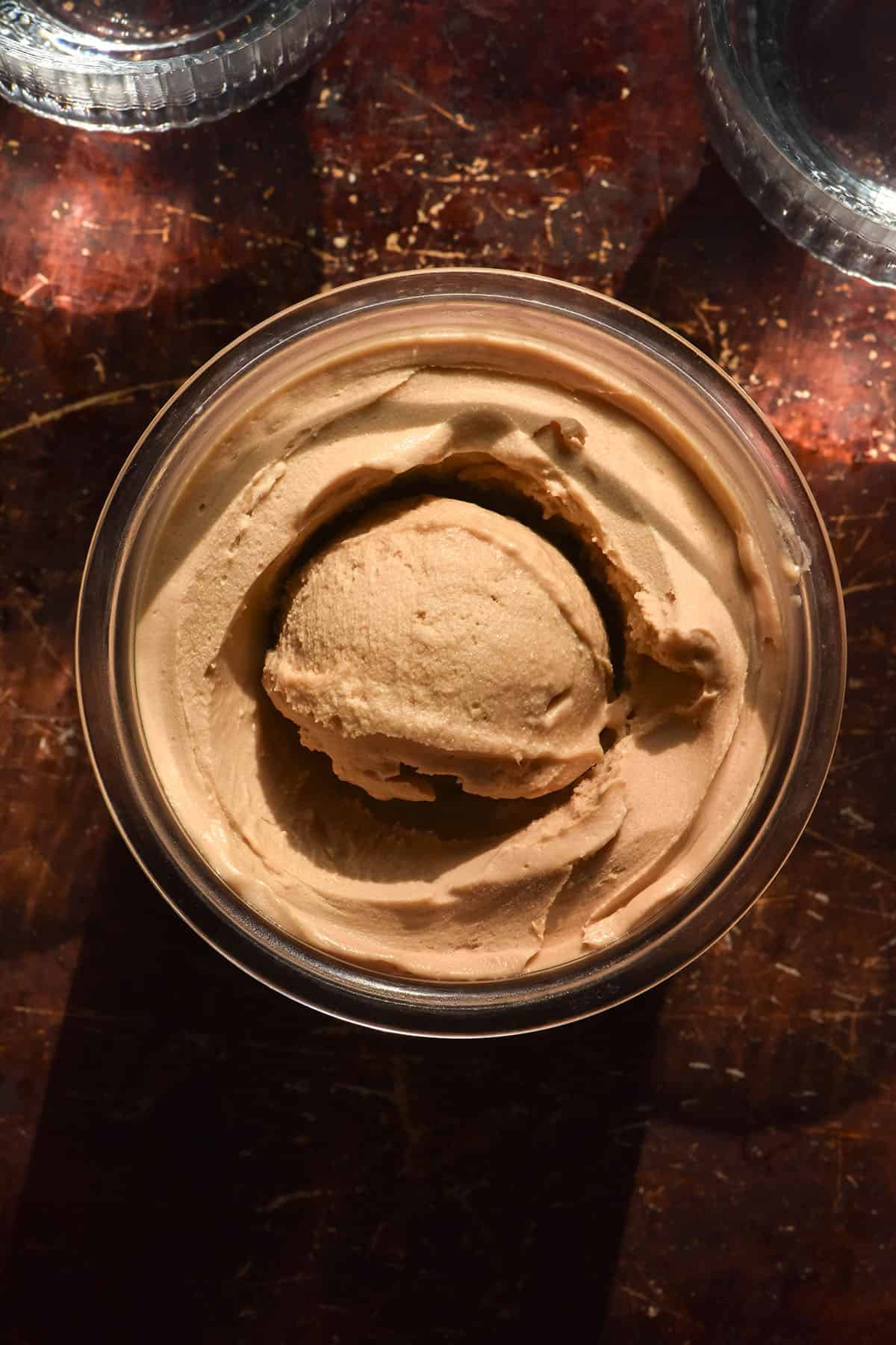An aerial image of a tub of vegan Ninja Creami Biscoff ice cream on a dark rust coloured backdrop