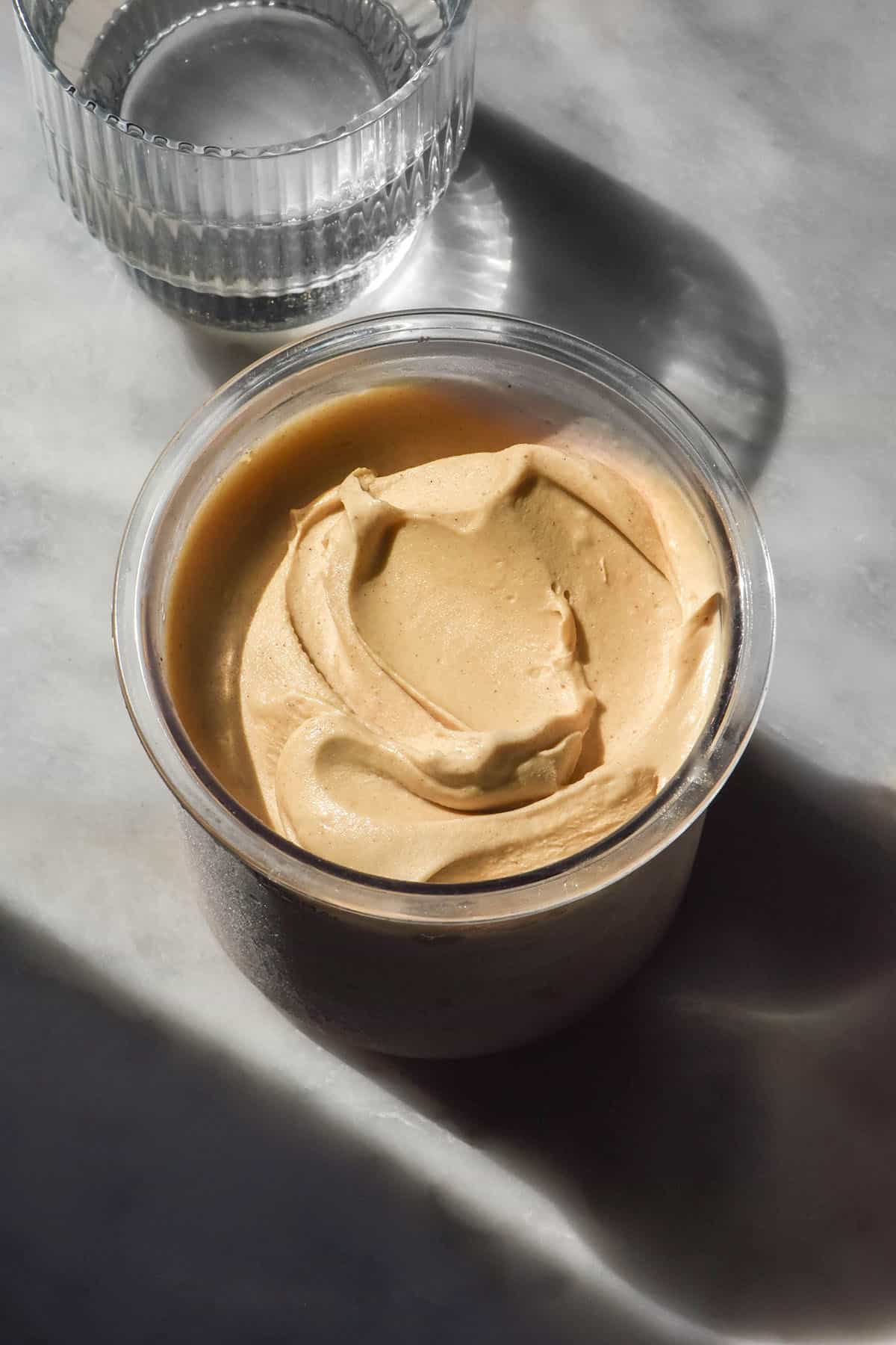 An aerial image of a tub of Ninja Creami gingerbread ice cream on a white marble table in contrasting sunlight
