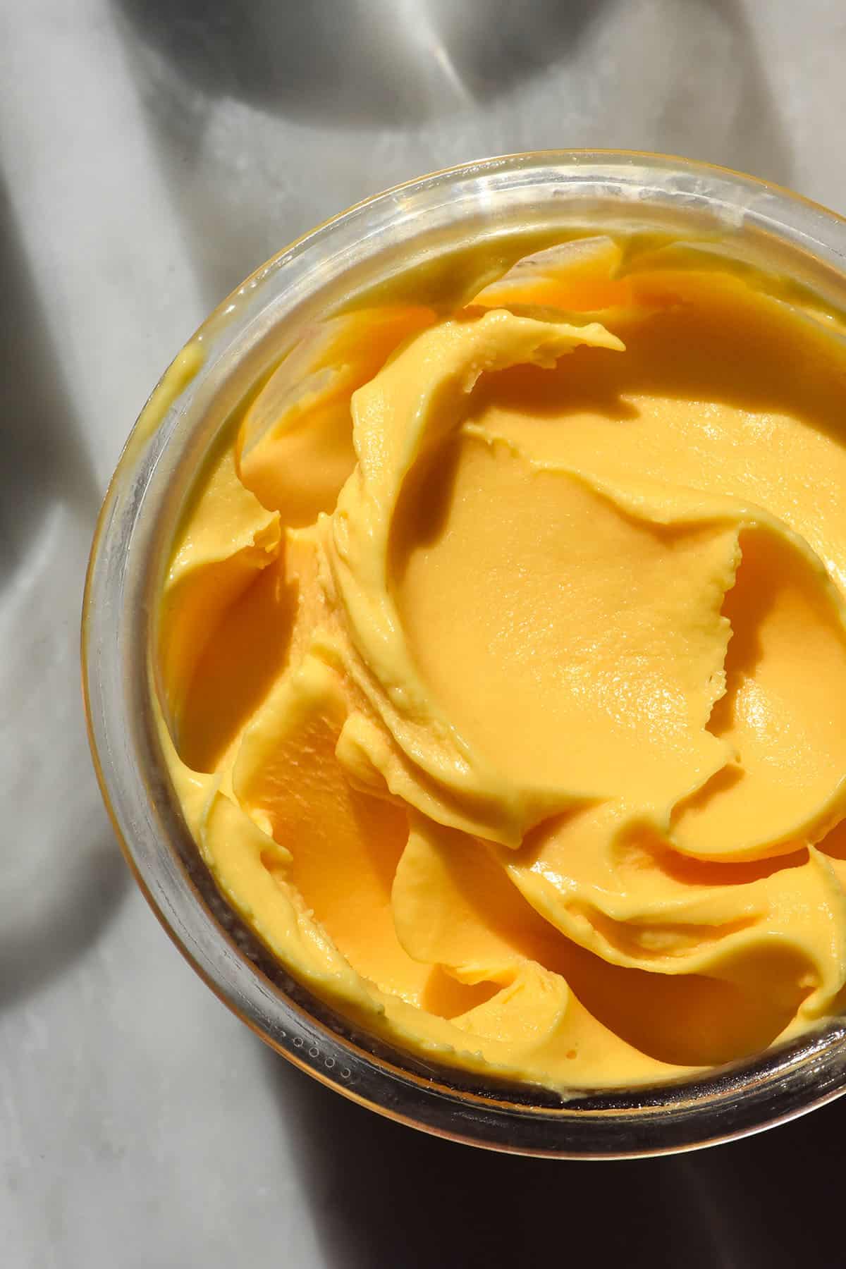 An aerial macro image of a tub of mango Ninja Creami ice cream on a sunlit white marble table.