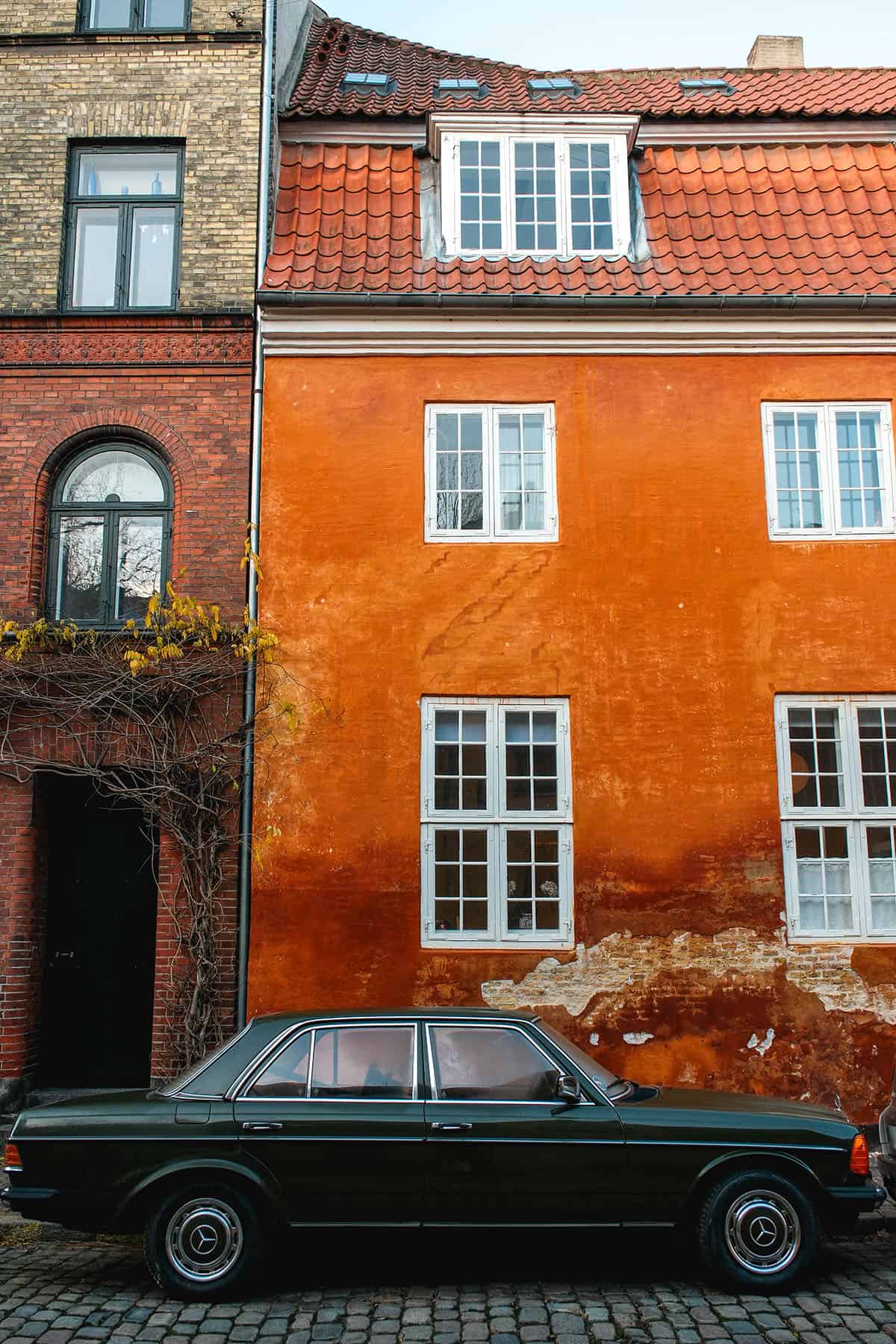 A vintage Mercedes set against contrasting rust orange and brick walls in Copenhagen, Denmark