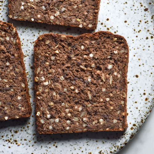 An aerial image of slices of gluten free seeded rye bread on a white speckled ceramic plate