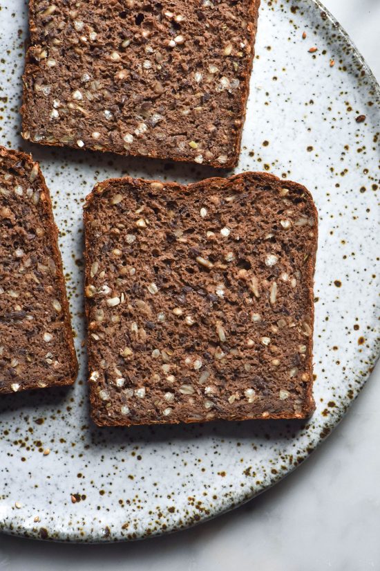 An aerial image of slices of gluten free seeded rye bread on a white speckled ceramic plate
