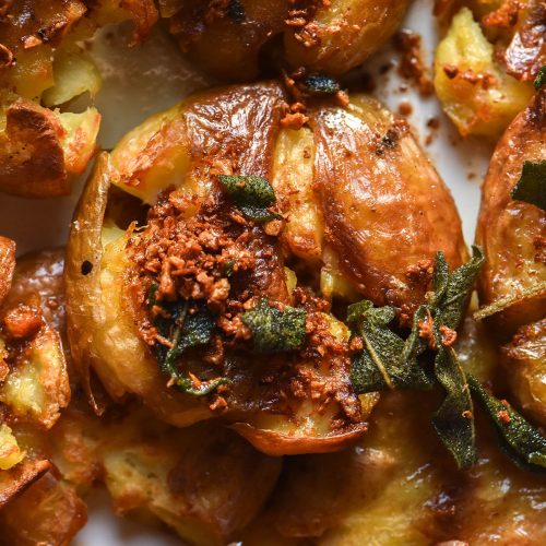 A close up macro image of crispy garlic sage potatoes on a white plate