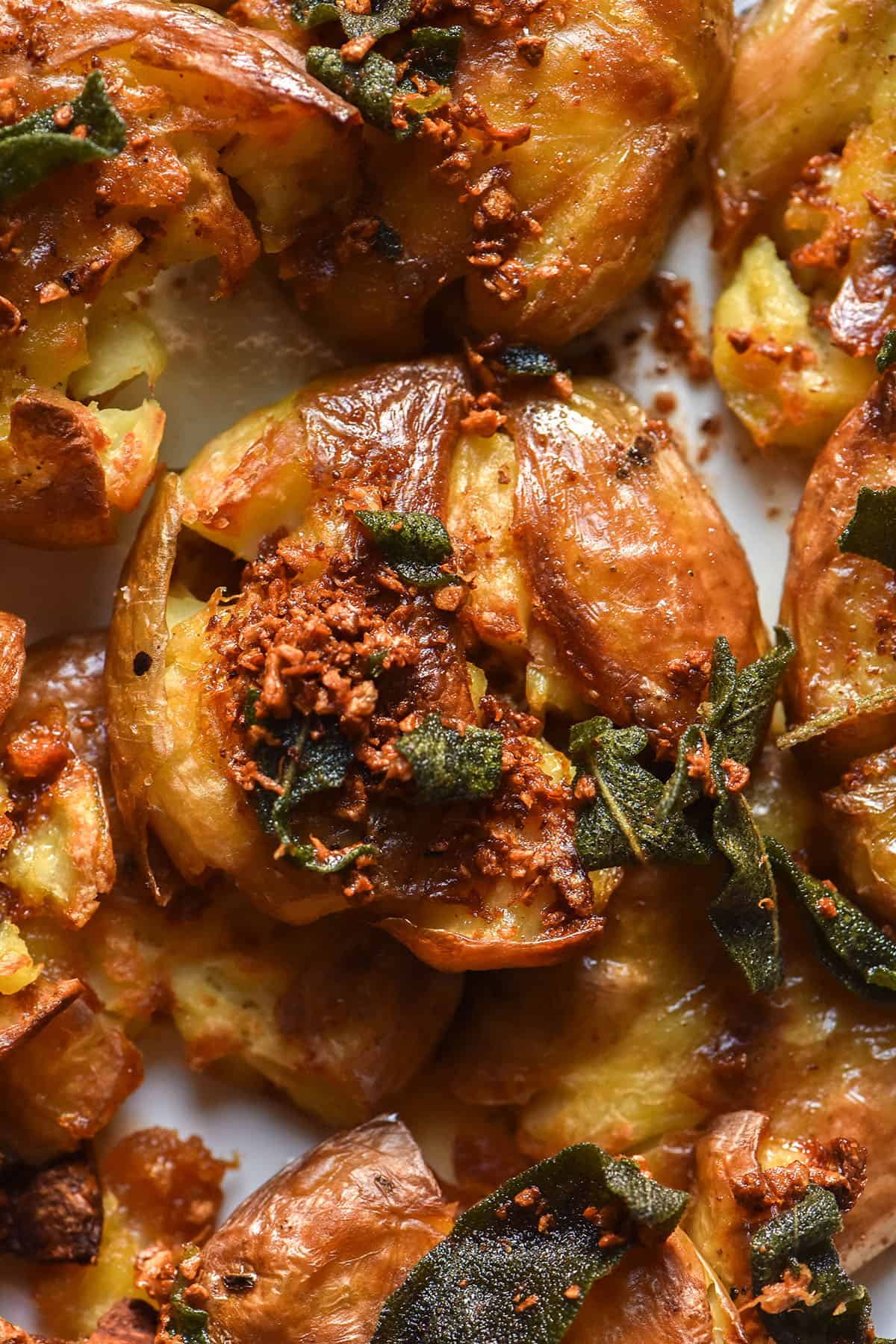 A close up macro image of crispy garlic sage potatoes on a white plate