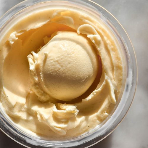 An aerial image of a tub of Ninja Creami custard ice cream on a sunlit white marble table