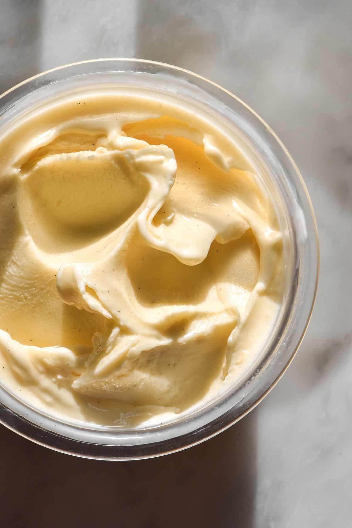 An aerial image of a tub of Ninja Creami custard ice cream on a brightly lit white marble table