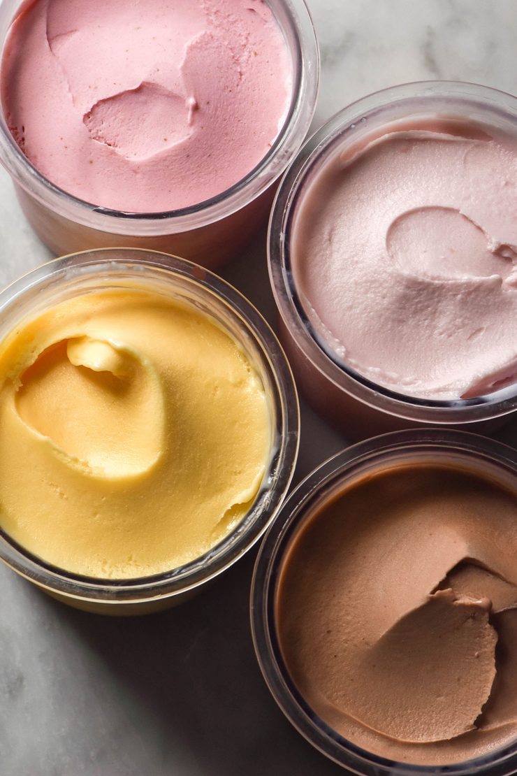 An aerial image of 4 tubs of Ninja Creami protein ice cream in various flavours. The tubs sit atop a white marble table.
