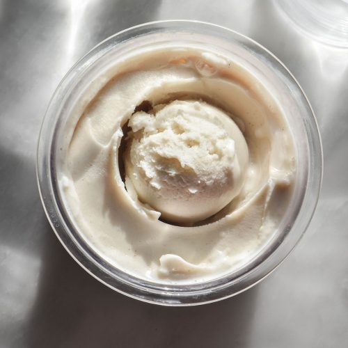 A brightly lit aerial image of a tub of Ninja Creami whey protein ice cream on a white marble table.