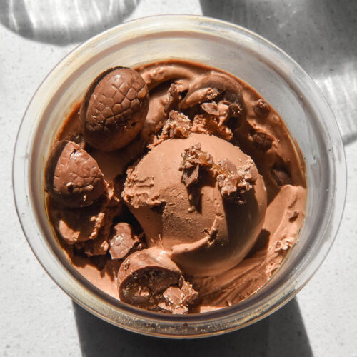 An aerial sunlit image of a tub of Ninja Creami chocolate caramel ice cream topped with chocolate caramel Easter eggs on a sunlit backdrop.