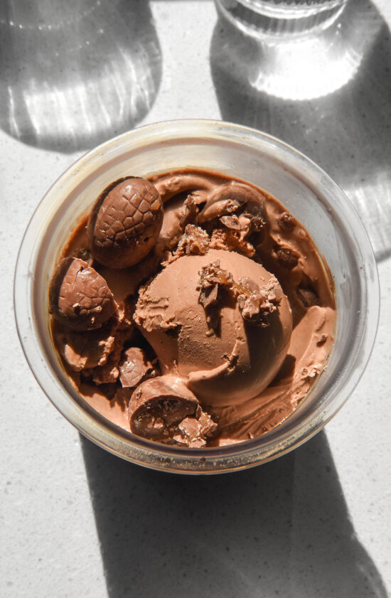 An aerial sunlit image of a tub of Ninja Creami chocolate caramel ice cream topped with chocolate caramel Easter eggs on a sunlit backdrop.
