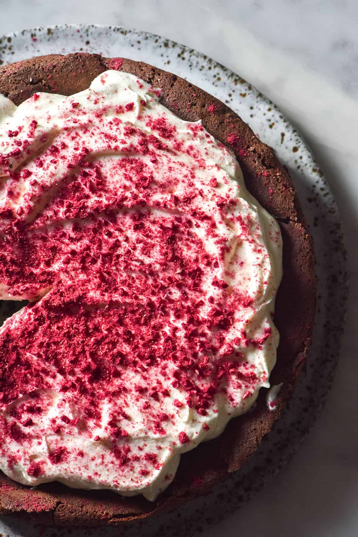 An aerial image of a dairy free flourless chocolate cake topped with whipped dairy free cream and freeze dried crushed raspberries.