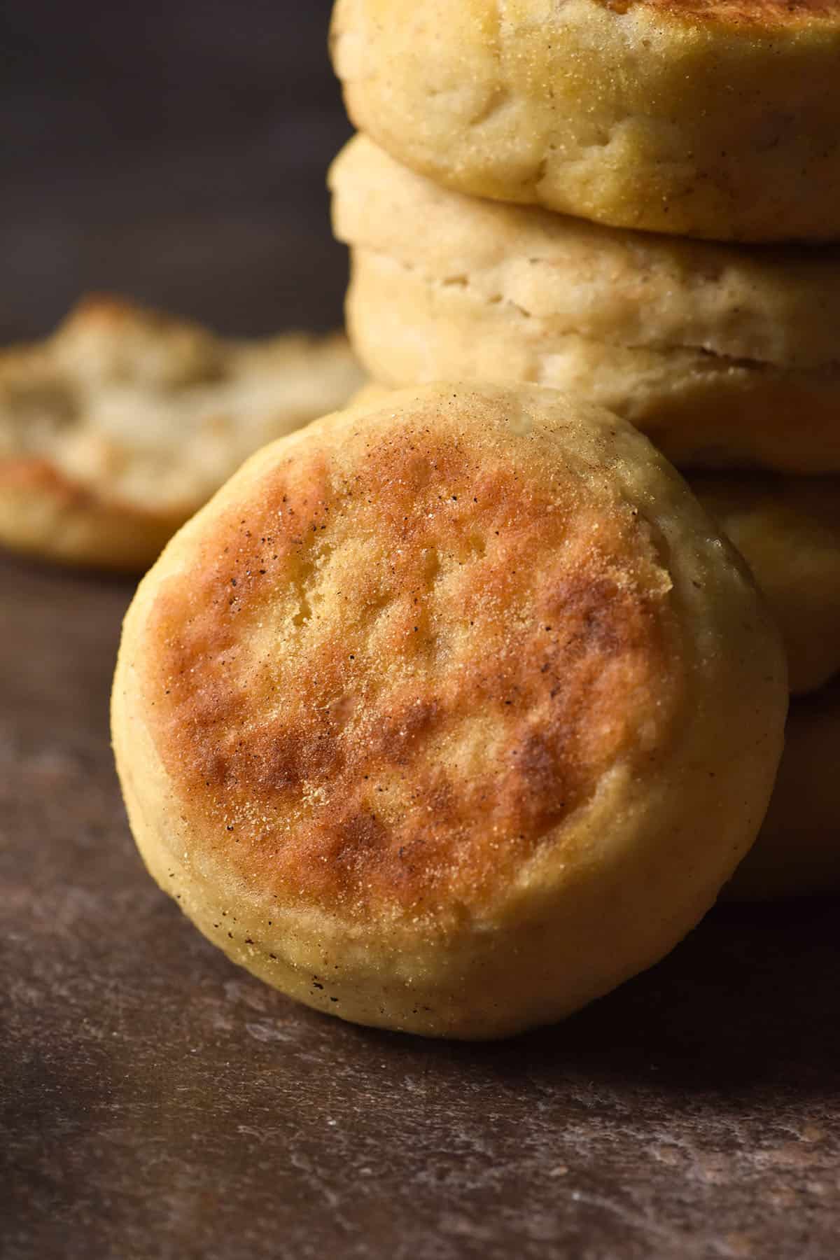 A side on image of a gluten free English Muffin stacked against other muffins against a dark backdrop