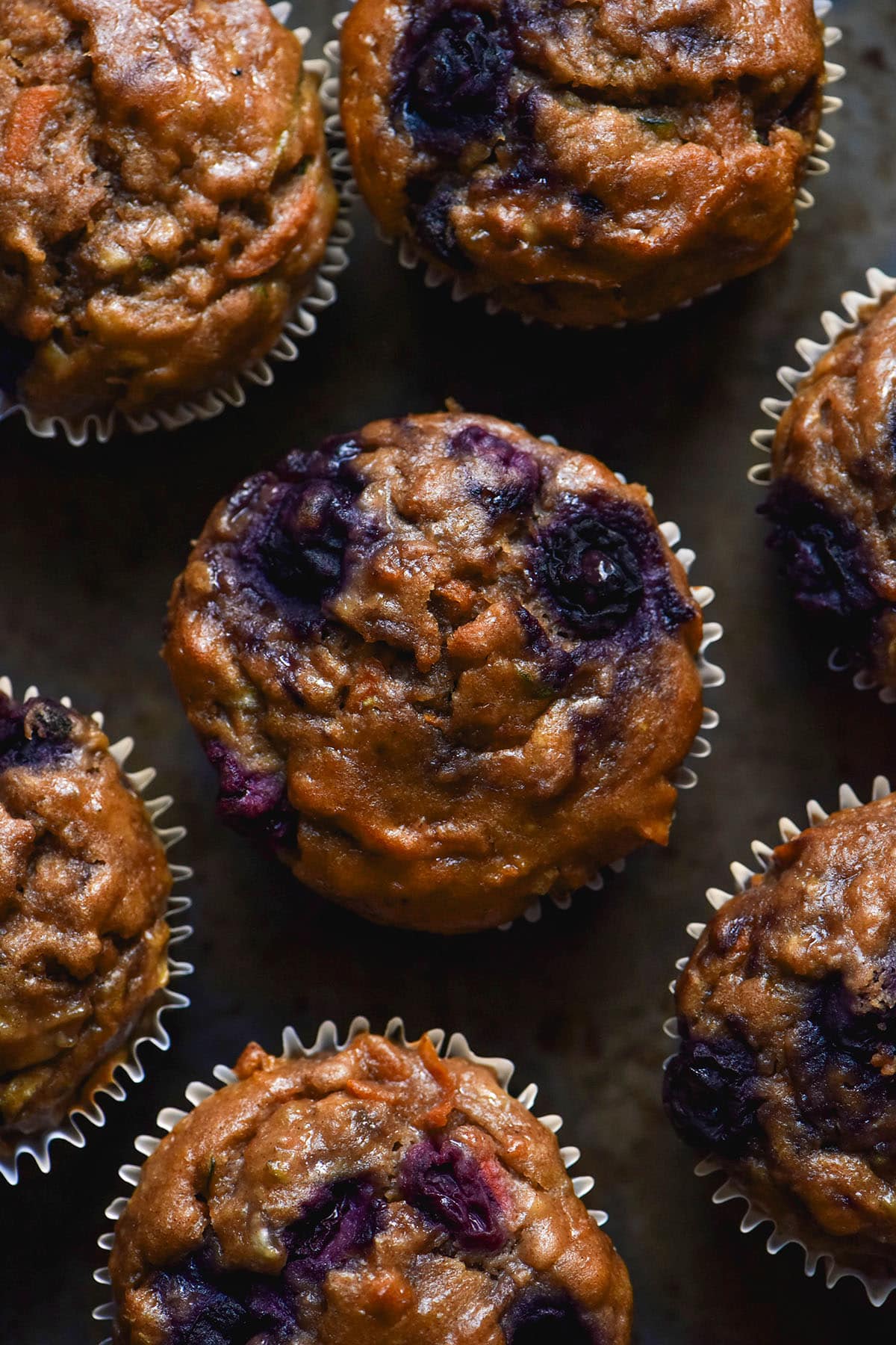 An aerial image of gluten free breakfast muffins studded with blueberries on a dark backdrop